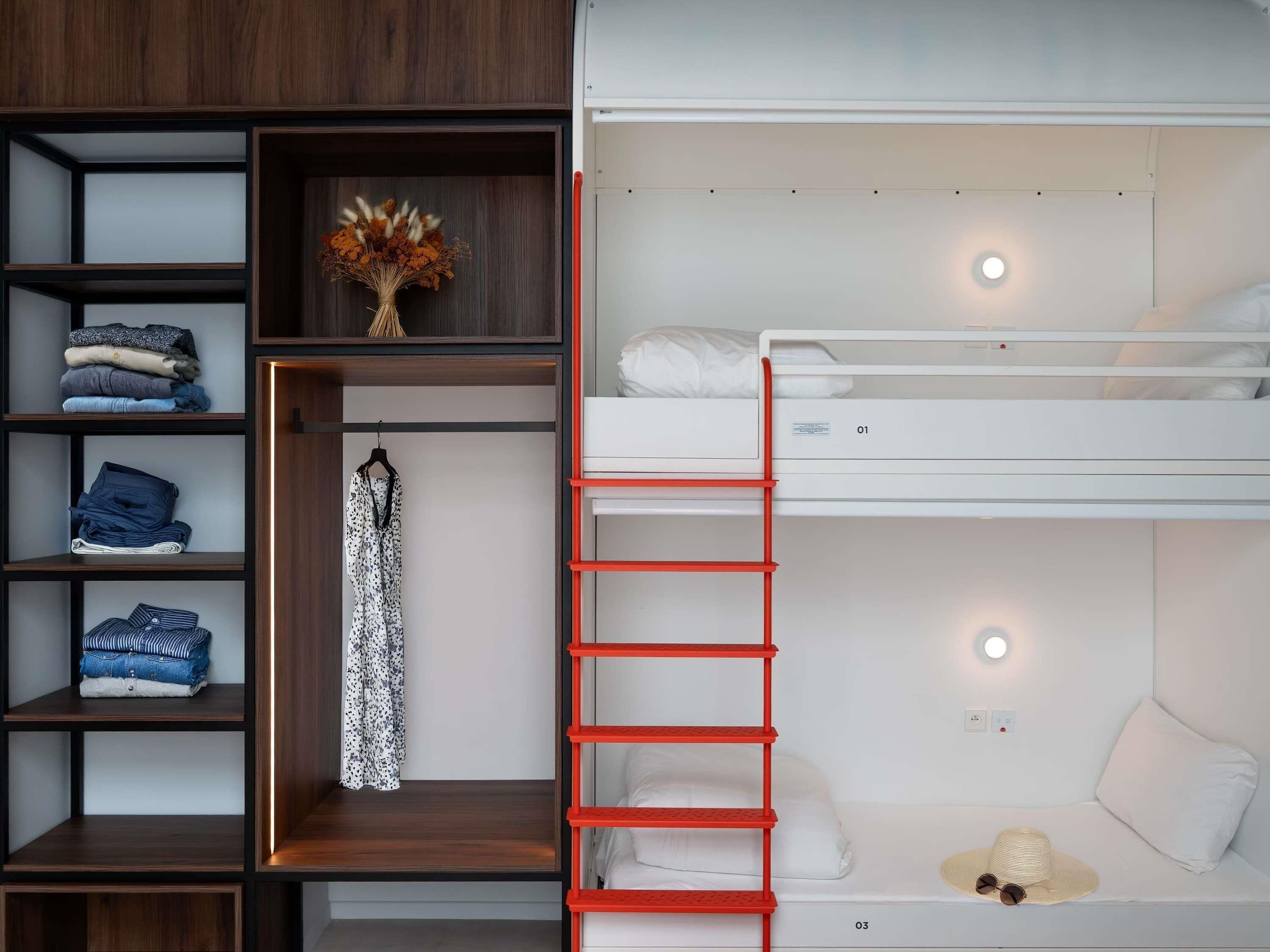 A bunk bed with a red ladder, a wardrobe with multiple shelves, and a hanging garment.