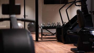 A gym with exercise equipment, a wooden floor, and a wall-mounted TV.