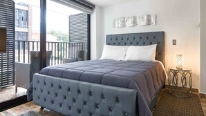 Een slaapkamer met een groot bed, een glazen tafel met een lamp en uitzicht op het balkon.