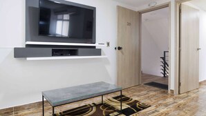 Een moderne woonkamer met een wandgemonteerde televisie, een glazen salontafel en een houten deur.
