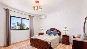 Un dormitorio con una cama de madera, dos mesitas de noche, un tocador, un aparador, un espejo y una ventana con cortinas.