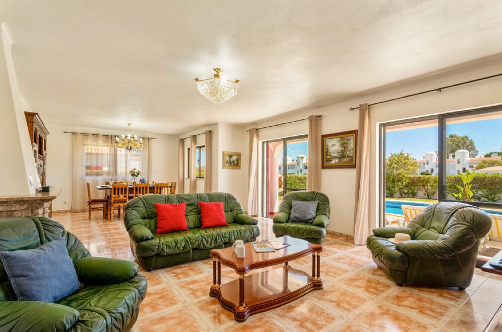 A spacious living room with green leather sofas, a wooden coffee table, and a dining area with a table and chairs.
