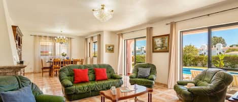 A spacious living room with green leather sofas, a wooden coffee table, and a dining area with a table and chairs.