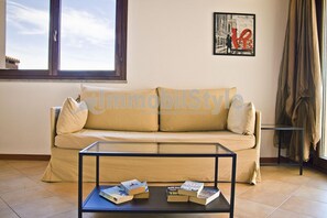 Una sala de estar con un sofá color beige, una mesa de centro de vidrio con libros, una ventana y un cartel con la palabra 'Love'.