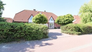 A red-tiled house with a white door and windows, surrounded by hedges and trees. - Cozy apartment with balcony for 4 people (Greetsiel)
