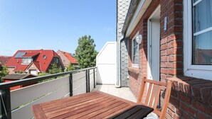 A balcony with a wooden table and a chair, a brick wall, and a window. - Cozy apartment with balcony for 4 people (Greetsiel)