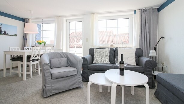 A modern living room with a grey sofa, a white coffee table, and a dining area with a white table and chairs. - Cozy apartment with balcony for 4 people (Greetsiel)