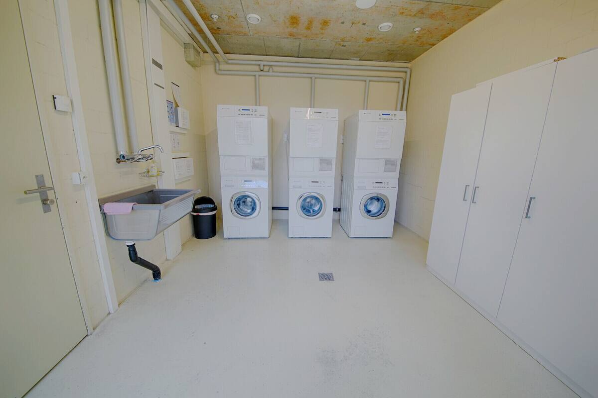 A laundry room with three stacked washing machines, a sink, and a trash can.