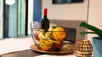 Un panier de fruits est posé sur une table, à côté d’une bouteille de vin et d’une bougie décorative.