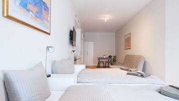 A modern, well-lit room with two beds, a desk, and a chair.