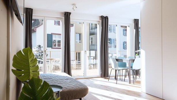 Una habitación moderna con un ventanal grande, una zona de comedor con sillas y una planta.