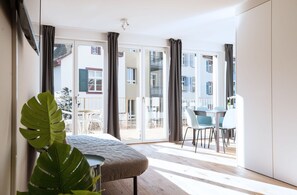 Une chambre moderne avec une grande fenêtre, un coin repas avec des chaises et une plante.