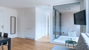 A modern living room with a glass partition, a flat-screen TV, and a dining area with a table and chairs. - BS Fox I - Messe Hitrental Apartment (Basel)
