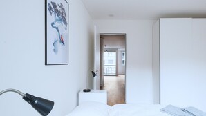 A modern bedroom with a bed, a desk, and a chair. There is a door leading to another room. - BS Fox I - Messe Hitrental Apartment (Basel)