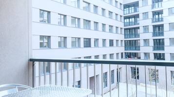A balcony with a metal table and chairs, overlooking a modern building with multiple windows.