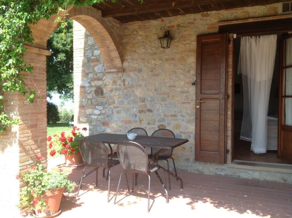 Un patio al aire libre con un muro de piedra, una puerta de madera y una mesa con sillas.