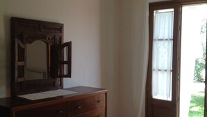 Une chambre à coucher avec une commode en bois, un grand miroir et un lit recouvert de linge de lit blanc.