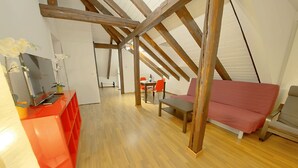 A loft-style room with wooden beams, a red sofa, a dining table with chairs, and a TV on a red stand. - ZH Strawberry - Oerlikon Hitrental Apartment (Zürich)