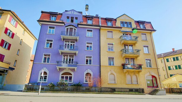 A multi-story building with balconies, a red door, and a visible street in front. - ZH Strawberry - Oerlikon Hitrental Apartment (Zürich)