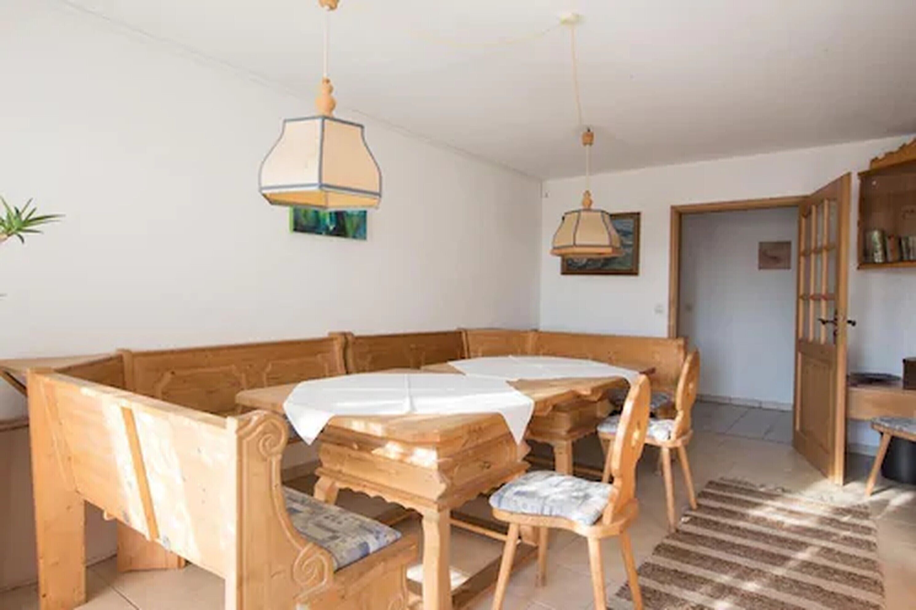 A dining area with a wooden table and benches, a hanging lamp, and a door leading to another room.