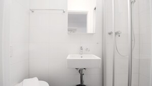 A bathroom with a white sink, a mirror, a toilet, and a glass-enclosed shower. - LU Station II - Hitrental Apartment (Lucerne)