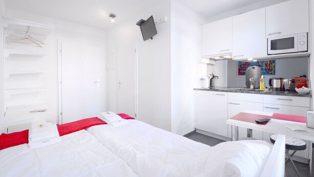 A hotel room with a bed, a desk, a microwave, and a small kitchenette. - LU Station II - Hitrental Apartment (Lucerne)