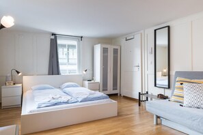 A modern bedroom with a large bed, a bedside table with a lamp, a wardrobe, a mirror, and a sofa. - ZG Zeughausgasse I - Hitrental Apartment (Zug)