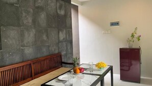 A dining area with a wooden bench and a glass table, a refrigerator, and a potted plant. - Bali Elephants Boutique Villa (Jimbaran)