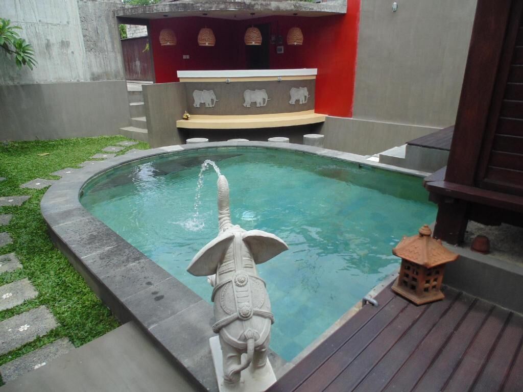 Ein Swimmingpool mit einer dekorativen Elefantenstatue, einer kleinen Laterne und einer roten Wand mit einer Bank.