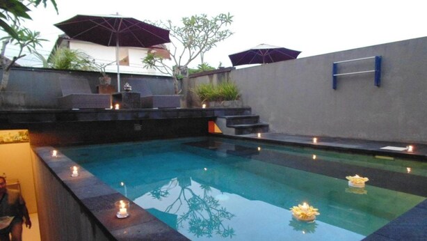 A swimming pool with candles along the edge, a small waterfall feature, and a concrete wall with a metal rack. - Bali Elephants Boutique Villa (Jimbaran)