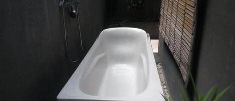 Eine moderne, rechteckige Badewanne in einem schmalen, geschlossenen Raum mit Fliesenboden und Ziegelwand.
