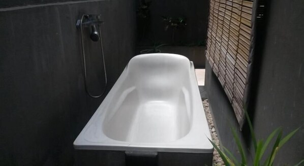 A modern, rectangular bathtub in a narrow, enclosed space with a tiled floor and a brick wall. - Bali Elephants Boutique Villa (Jimbaran)