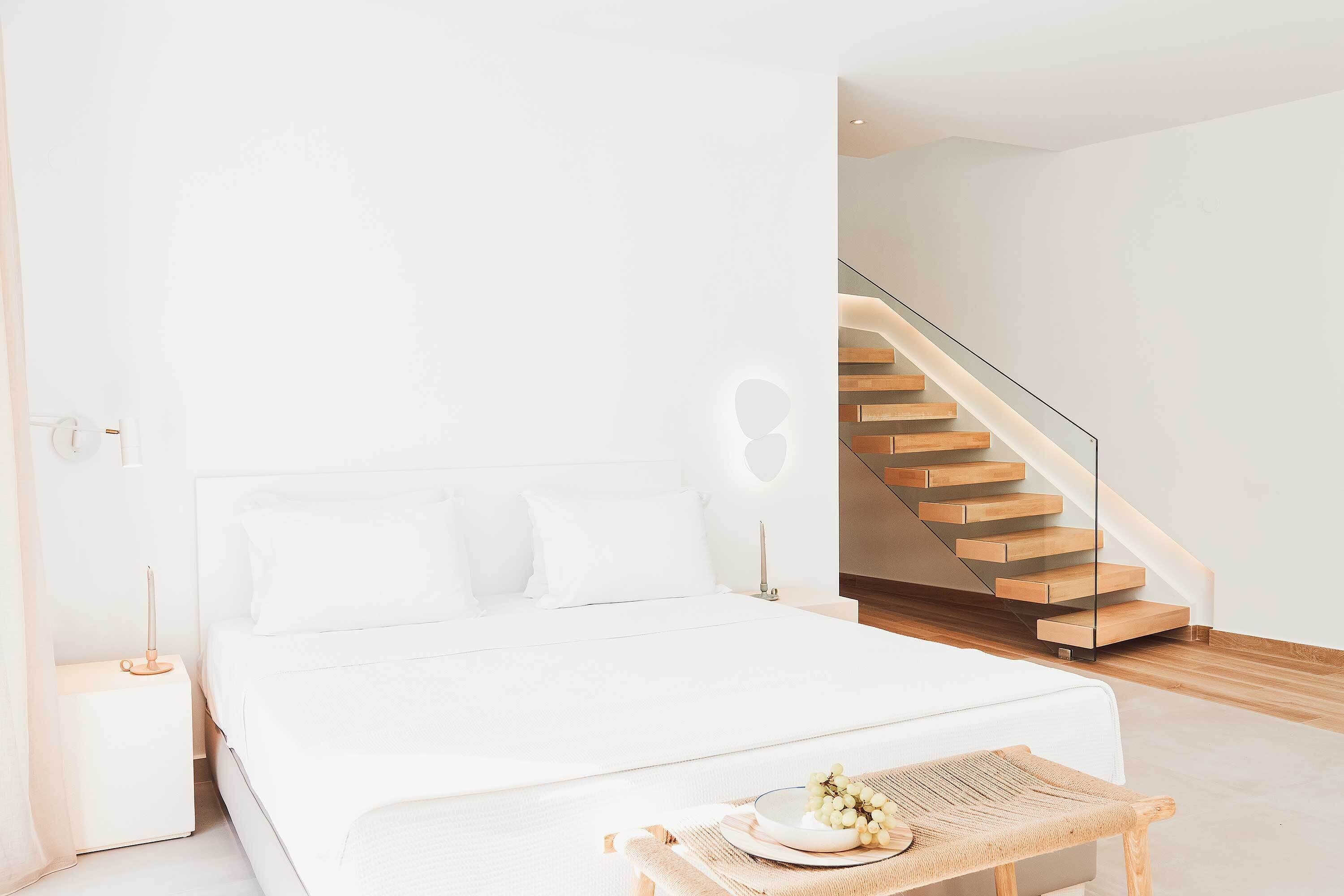 Ein modernes Schlafzimmer mit einem großen Bett, einem Nachttisch, einer Stehlampe und einer an der Wand befestigten Leuchte sowie einer Holztreppe.