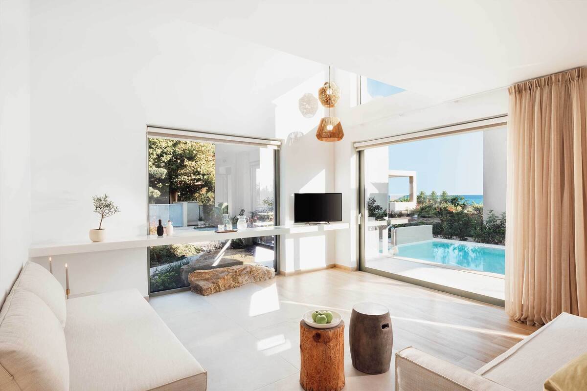 Un salon moderne doté d’une grande fenêtre donnant sur une piscine et la mer.