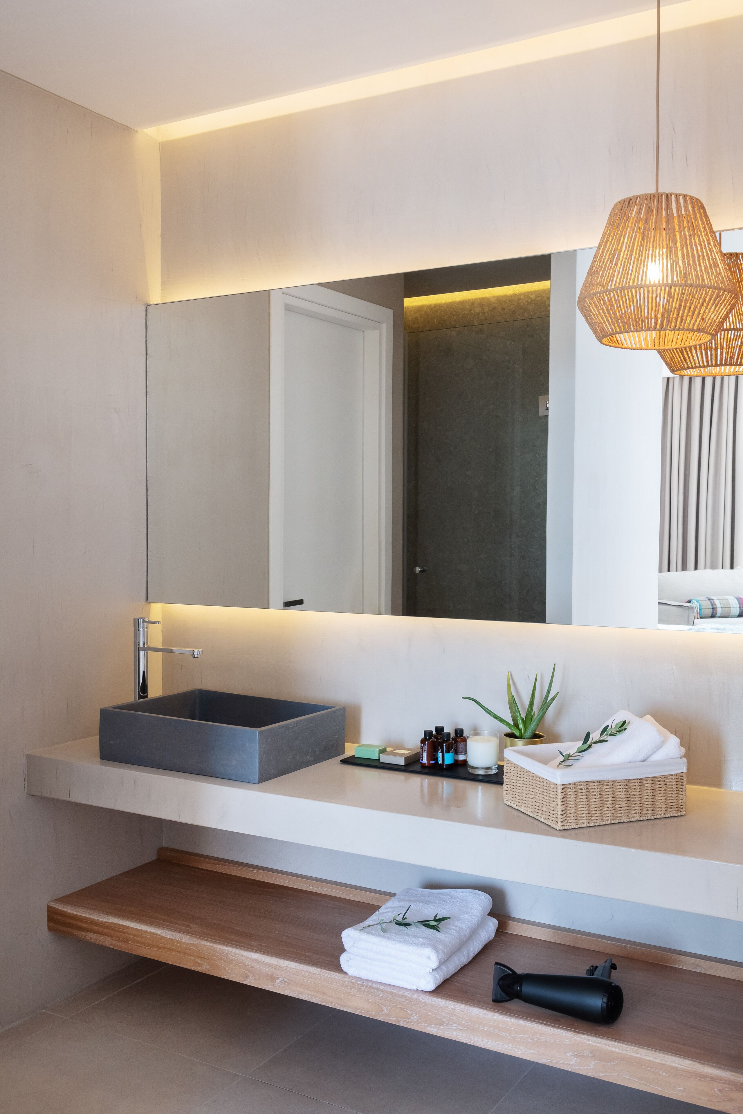 Un baño moderno con un espejo grande, un lavamanos rectangular y un estante de madera con toallas.