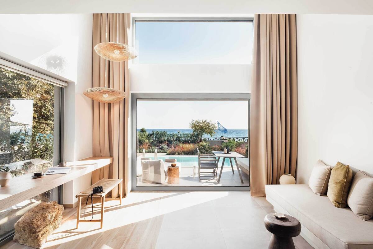 Un salon moderne doté d’une grande fenêtre, d’un canapé, d’un coin repas et offrant une vue sur la mer.