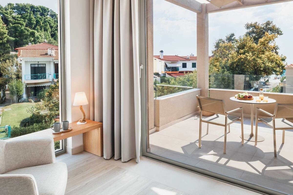 Un balcon avec une table et des chaises, une lampe, et une vue sur les bâtiments et la végétation environnants.