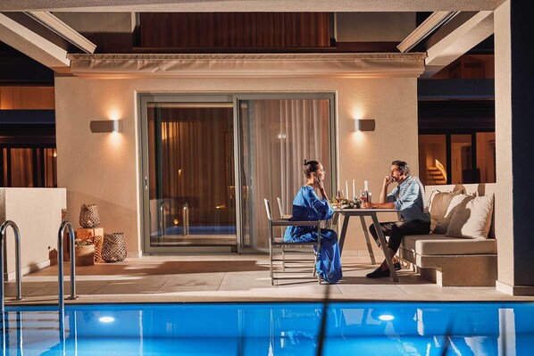 A poolside area with a glass door, a table with two people, and a sofa. - Cavo Delea Villas And Suites (Kassandra)