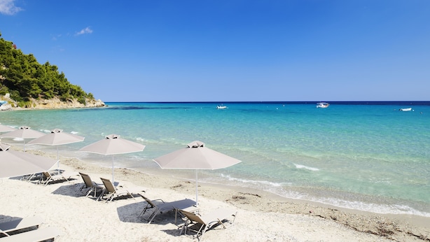 Una playa con agua turquesa cristalina, varias sombrillas y sillas de playa.