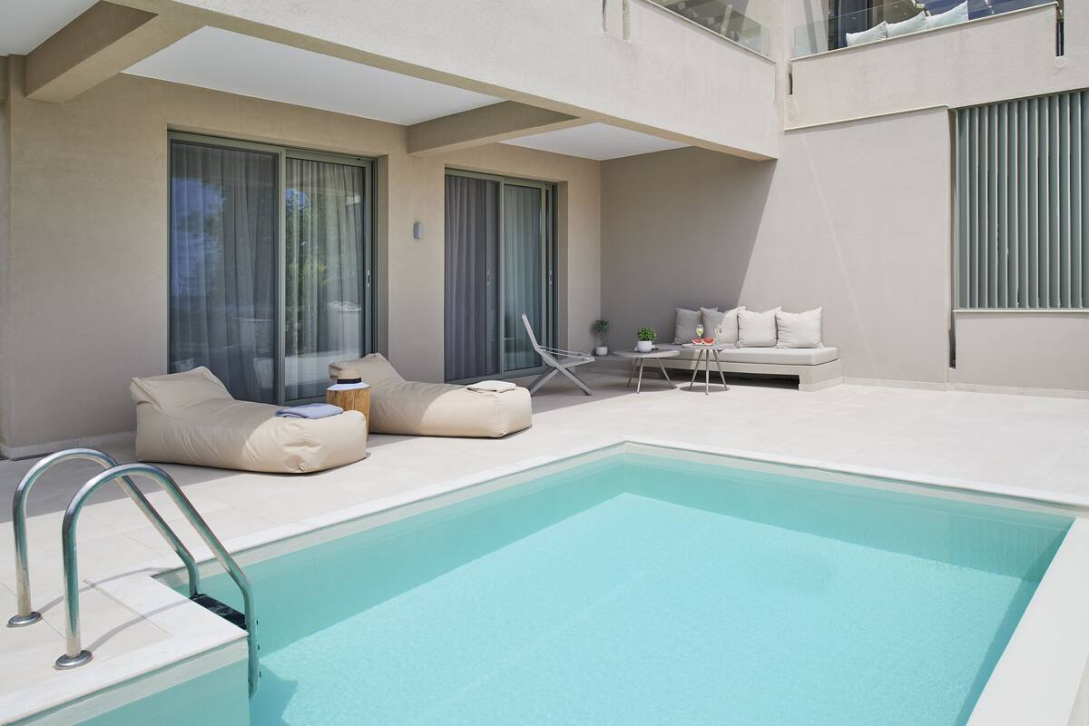 Un espace piscine extérieur moderne, doté d’un design minimaliste, comprenant une piscine, des chaises longues et une petite table agrémentée d’une plante.