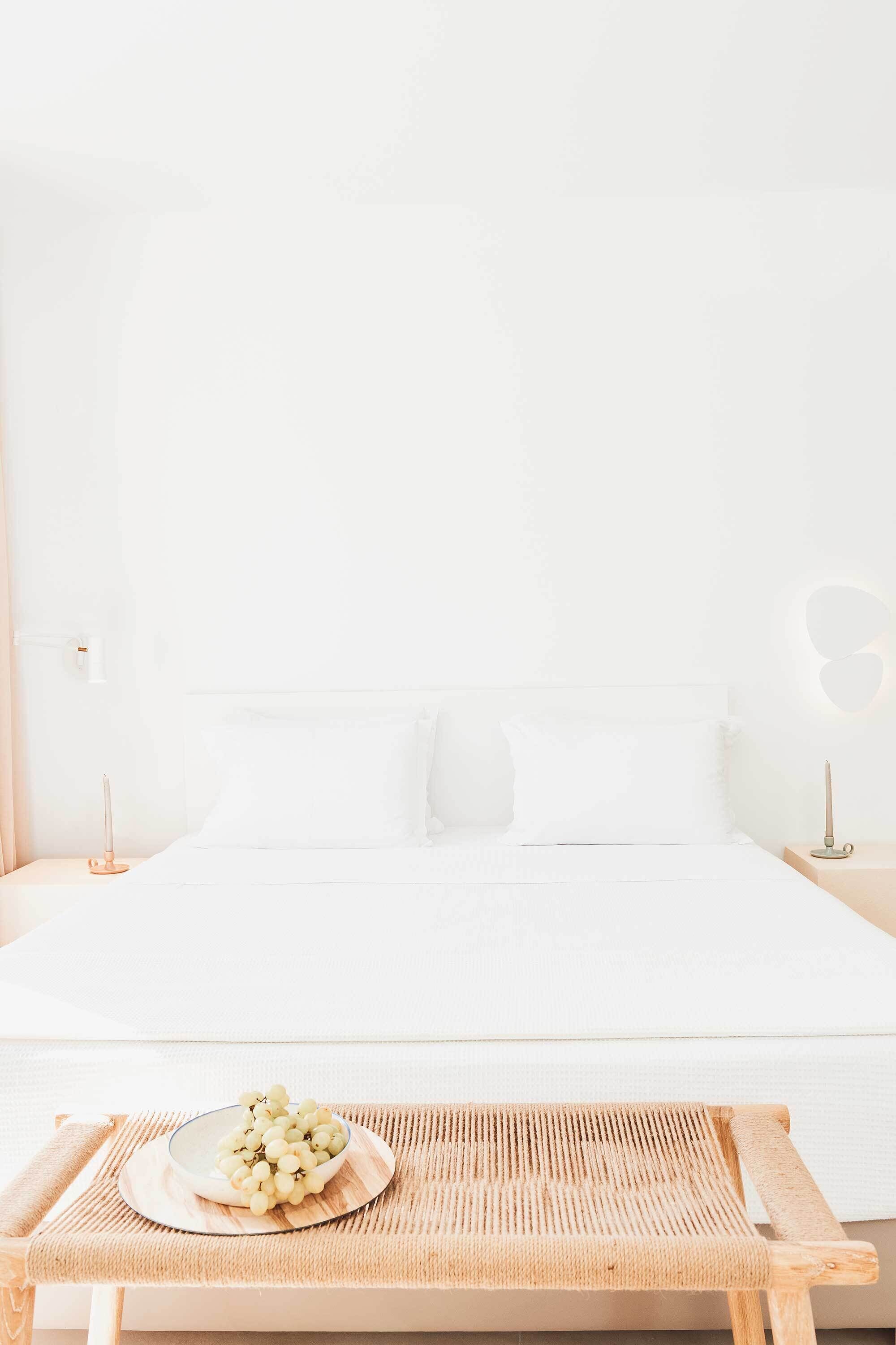 A bedroom with a bed, bedside tables, a bedside lamp, a tray with a bowl of grapes, and a woven mat.