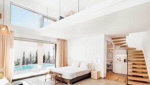 Un dormitorio moderno con un ventanal grande, una cama, una mesita y una escalera.