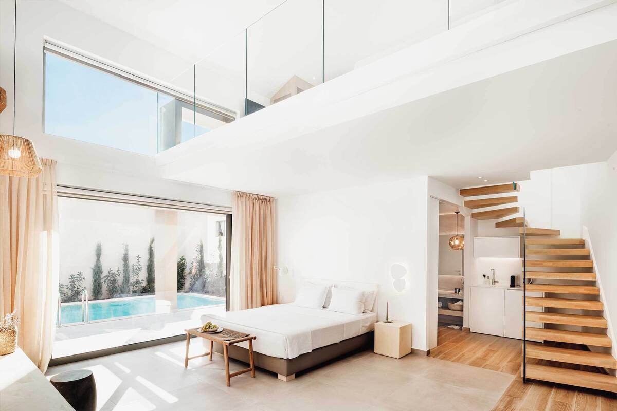 Une chambre moderne avec une grande fenêtre, un lit, une petite table et un escalier.