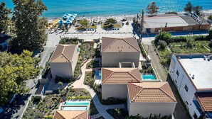Un complejo turístico frente al mar con varias construcciones, cada una con techo de tejas y piscina.