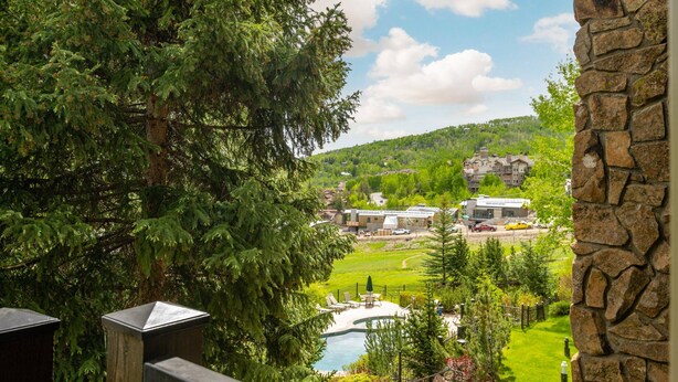 A view of a resort with a pool, surrounded by lush greenery and a mountainous backdrop. - Summer Haven in Snowmass! Stunning Balcony Views, Pool/Hot Tub, Wood FP, Sleeping Den, W/D & Parking (Snowmass Village)