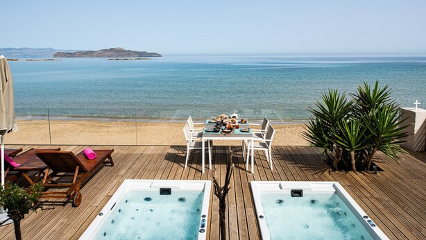 A wooden deck with two hot tubs, a table with chairs, and a view of the sea. - Beachfront luxury villa with hot tub & sunset view (Chania)