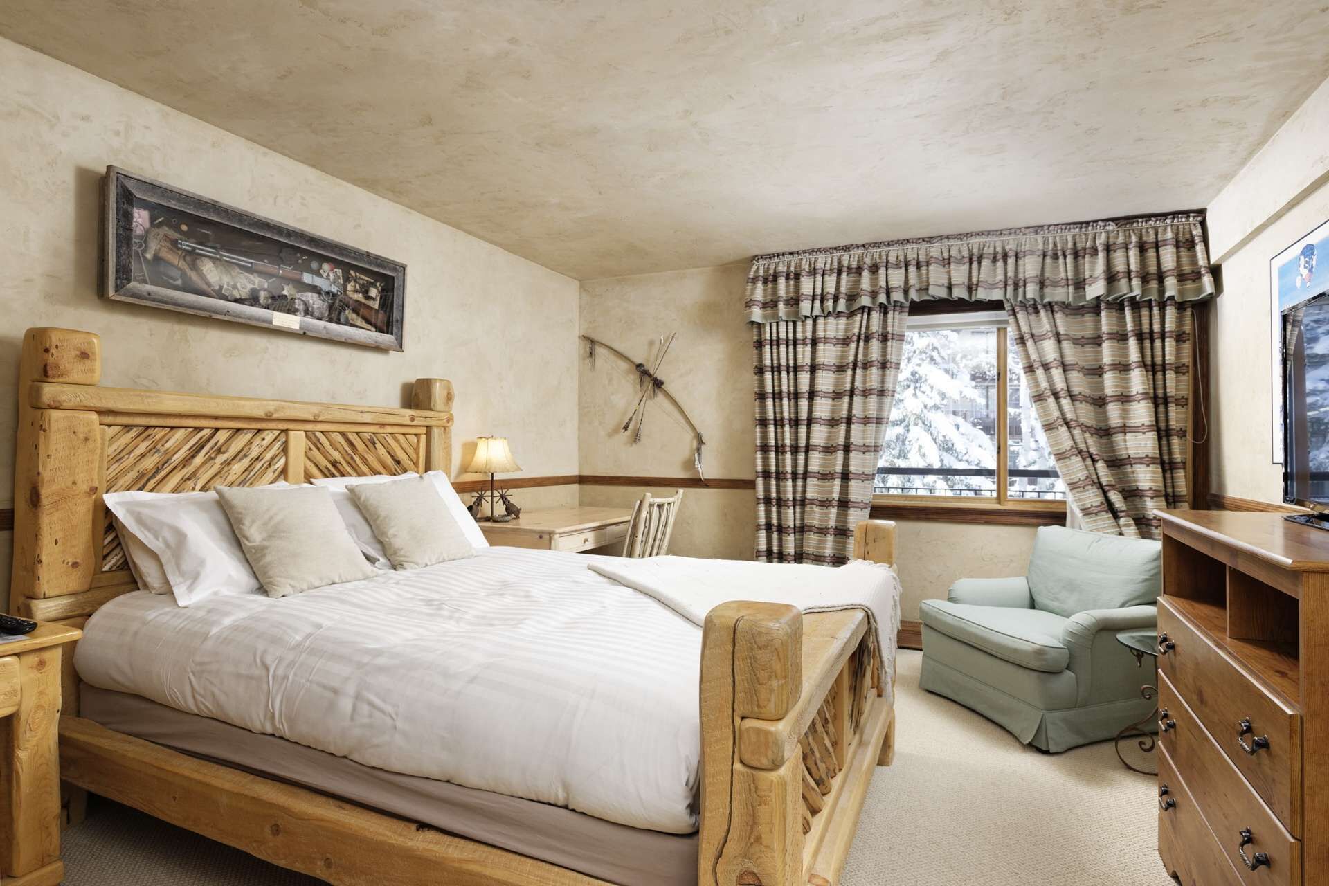 A bedroom with a wooden bed, a desk, a chair, a dresser, and a window with curtains.