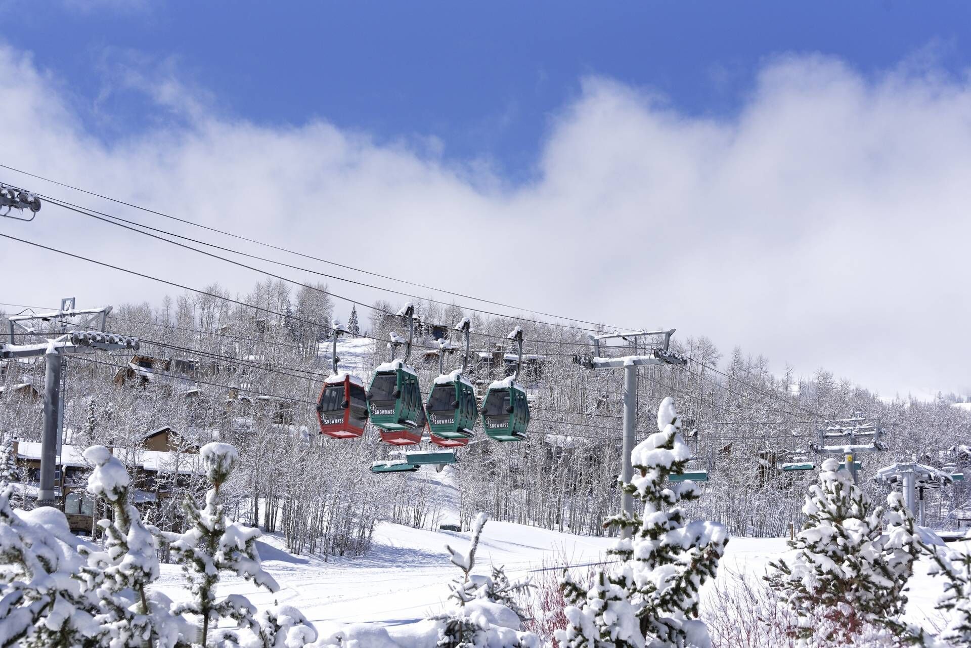 Un telesilla con cabinas que indican "Snowmass" con un paisaje de montaña nevada.