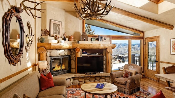 A cozy living room with a stone fireplace, leather furniture, and a view of mountains through large windows. - Beautiful Snowmass Getaway! Scenic Views, Balcony, Pool, Hot Tub, Gas FP, Elevator & Trail Access (Snowmass Village)