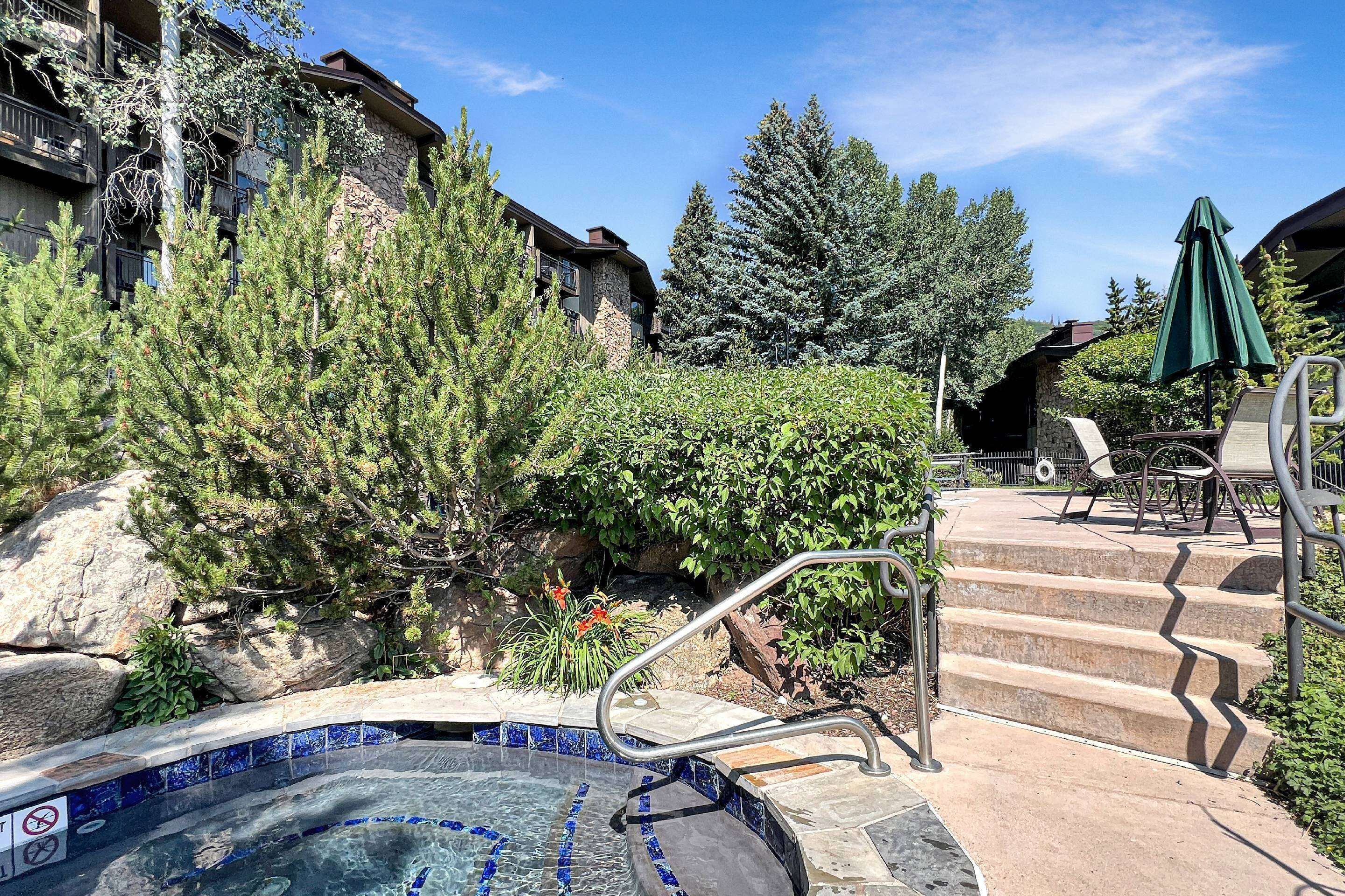 A hot tub area with stone steps leading up to it, surrounded by trees and a stone building.
